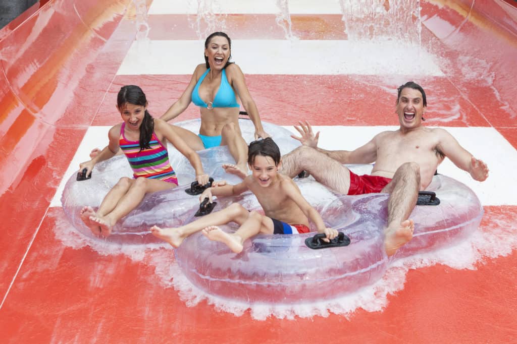 A happy family of mother, father and children, son and daughter, having fun on vacation on a slide at a waterpark